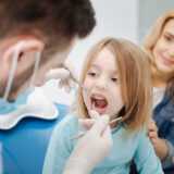 Nice good tempered patient child paying a regular visit to her doctor and sitting still with her mouth open while he examining her teeth.