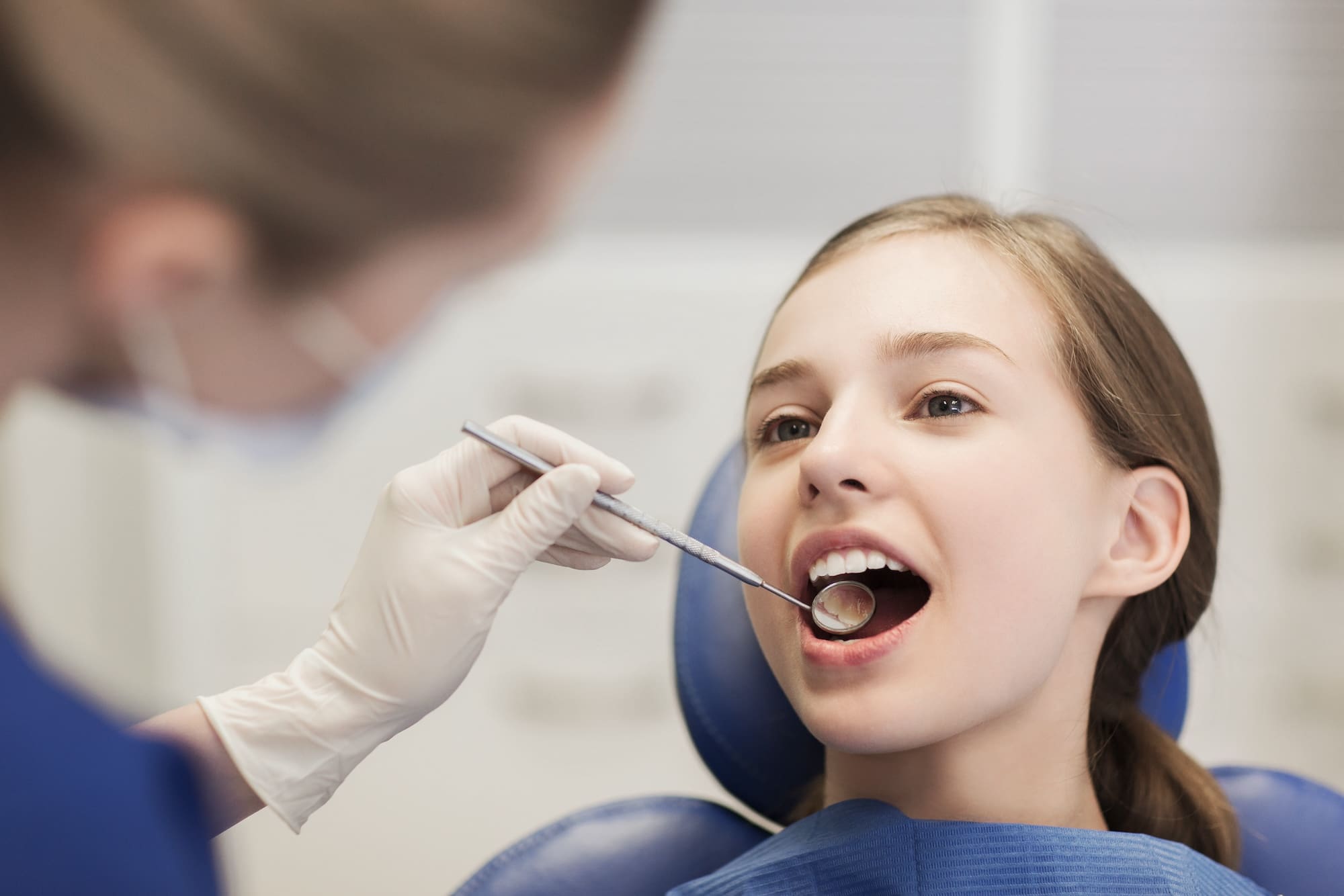 people, medicine, stomatology and health care concept - happy female dentist with mirror checking patient girl teeth up at dental clinic office